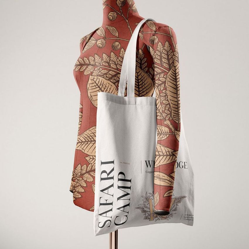 Tote bag mockup featuring a white fabric bag with black text and a botanical illustration, displayed on a patterned mannequin.
