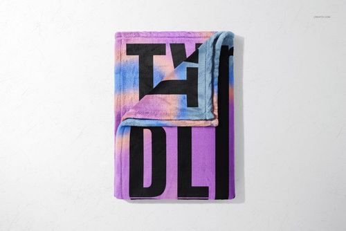 Folded fleece blanket mockup featuring large black typography over a purple and pastel gradient, viewed from above.
