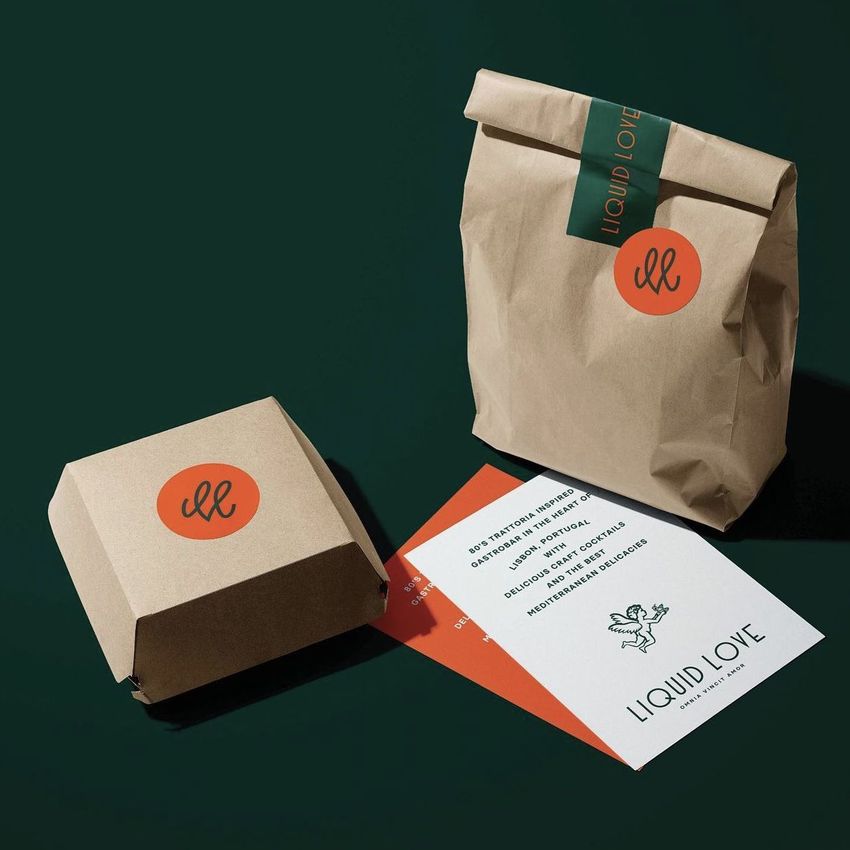Sticker mockup featuring a brown paper bag and box with round orange stickers, two cards, and a dark green background.