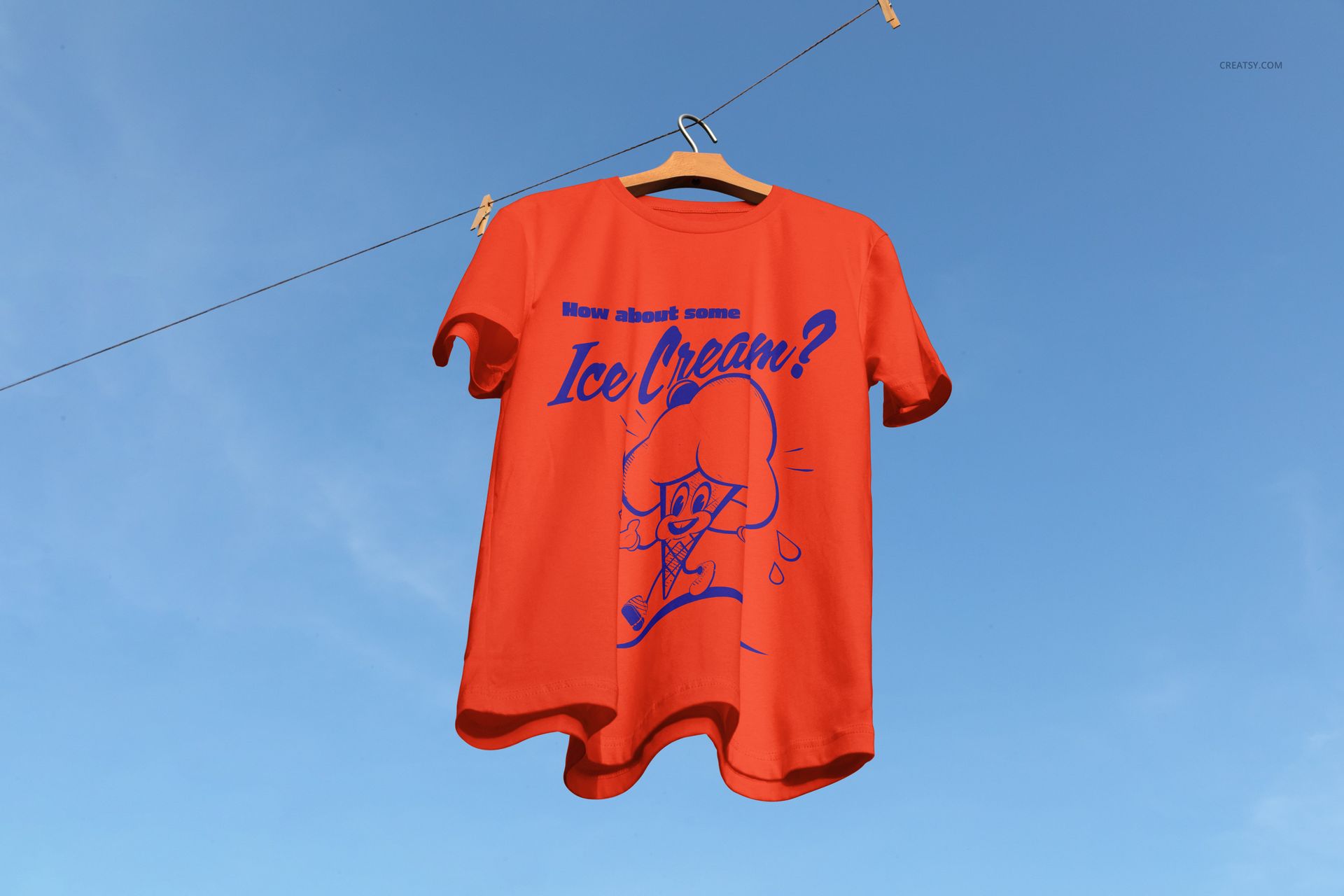 PSD mockup of a red short sleeve t-shirt with playful blue illustration, displayed outdoors against a sunny sky.