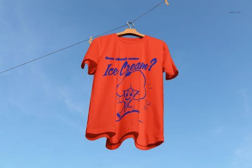PSD mockup of a red short sleeve t-shirt with playful blue illustration, displayed outdoors against a sunny sky.