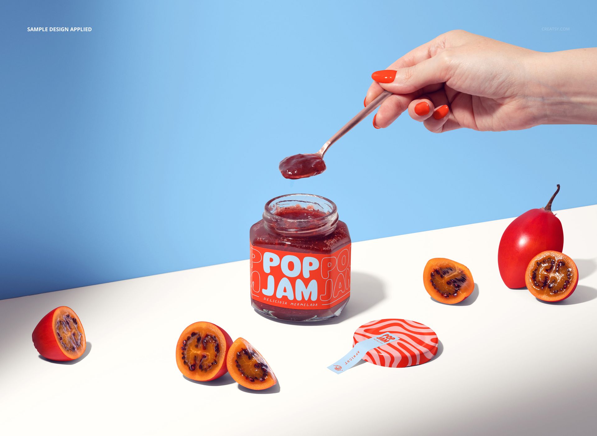 Glass tamarillo jam jar mockup on a light surface, with sliced tamarillos, jar lid, and a hand scooping jam.