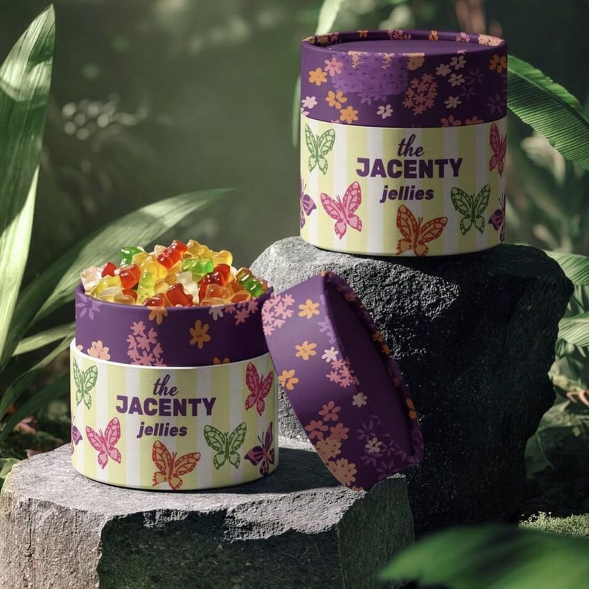 Paper tubes packaging mockup for jellies, featuring colorful butterfly patterns and text, placed on rocks in a lush jungle setting.