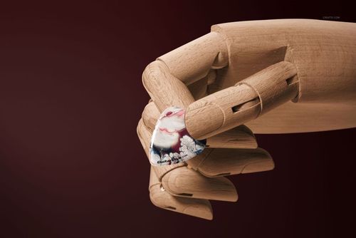 PSD mockup featuring a guitar pick with artistic design held by a wooden hand, set against a dark red background.