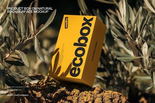 Yellow packaging box mockup featuring black lettering, displayed outdoors on a rocky surface with leafy branches.