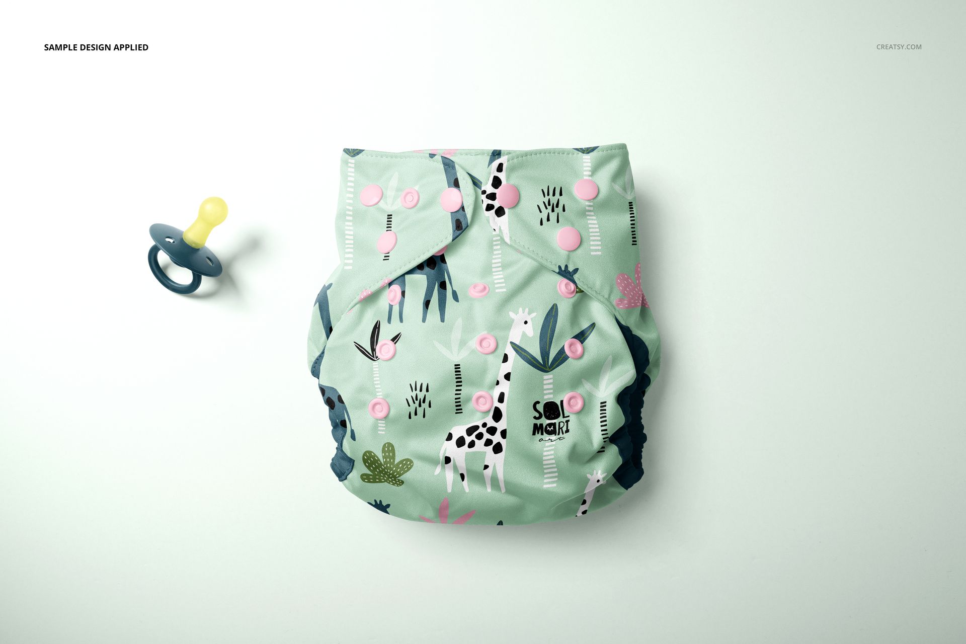 Top view of a reusable baby cloth diaper mockup with playful giraffe and foliage patterns, next to a pacifier.