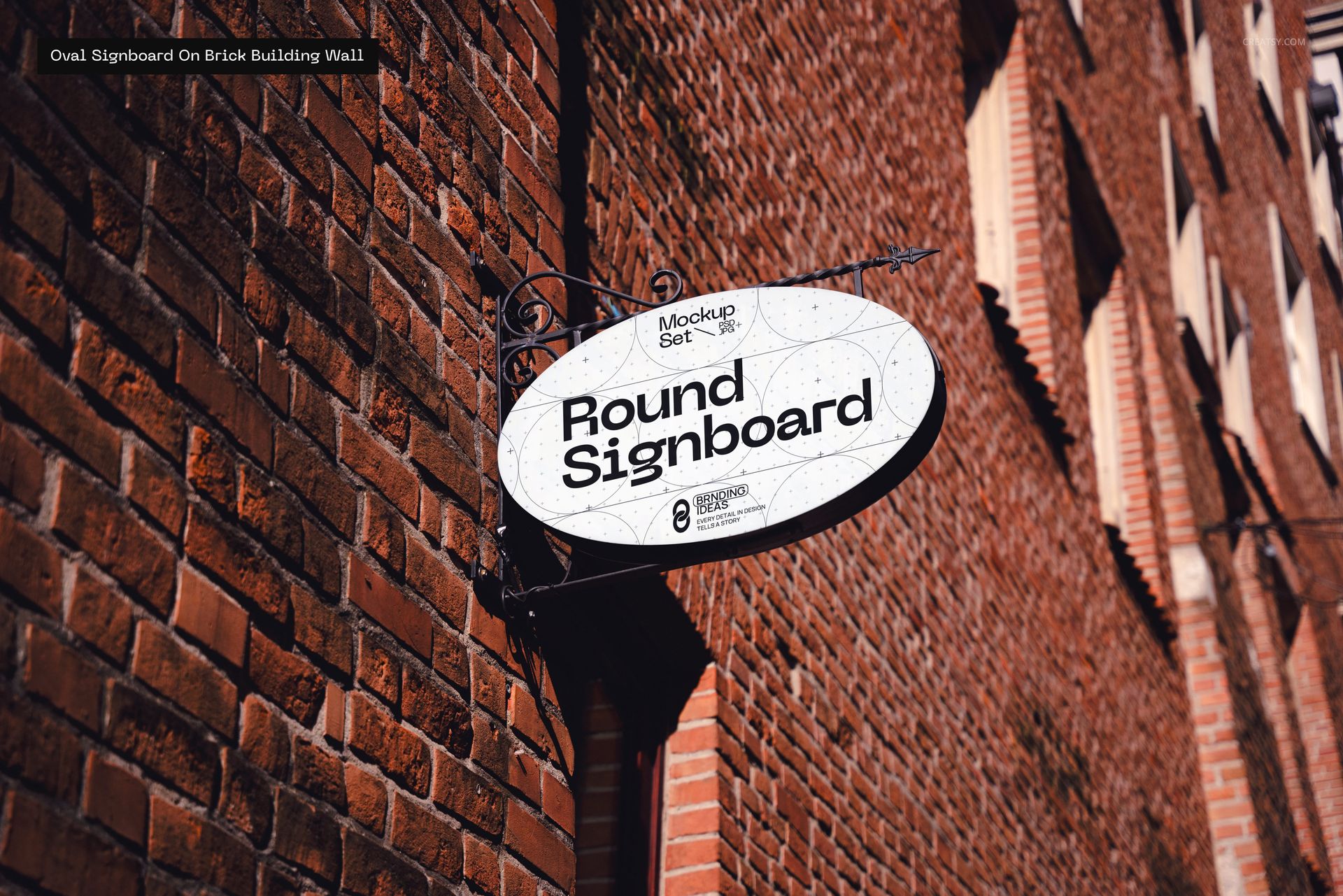 Oval signboard mockup mounted on a red brick building wall, photographed from a side angle in natural light.