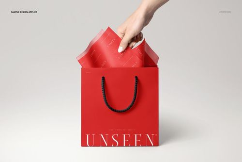 PSD mockup showing a hand inserting red patterned tissue paper into a red shopping bag, photographed from the front.