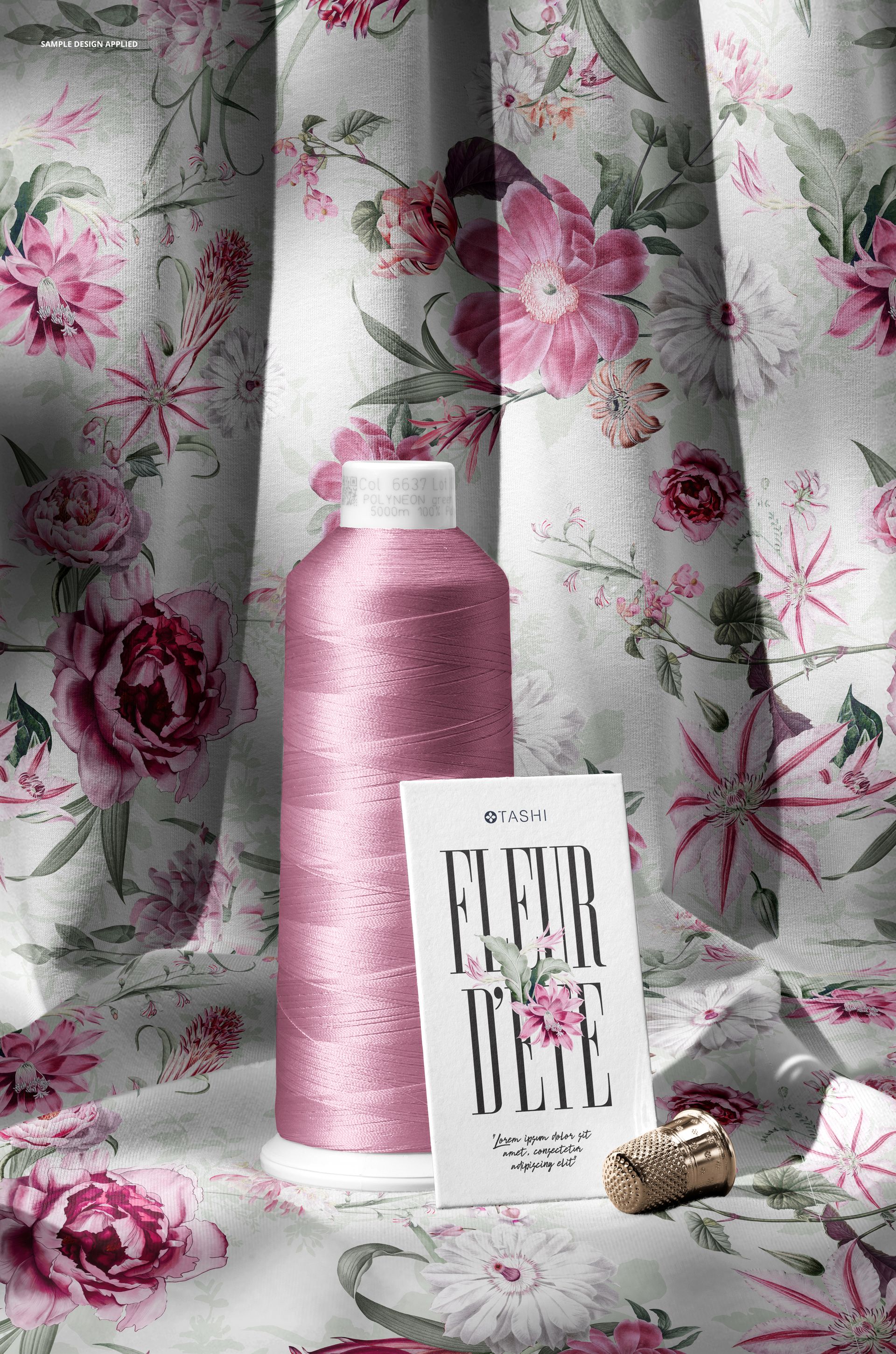 PSD mockup featuring a pink thread spool, metallic thimble, and card on draped jersey fabric with floral design.