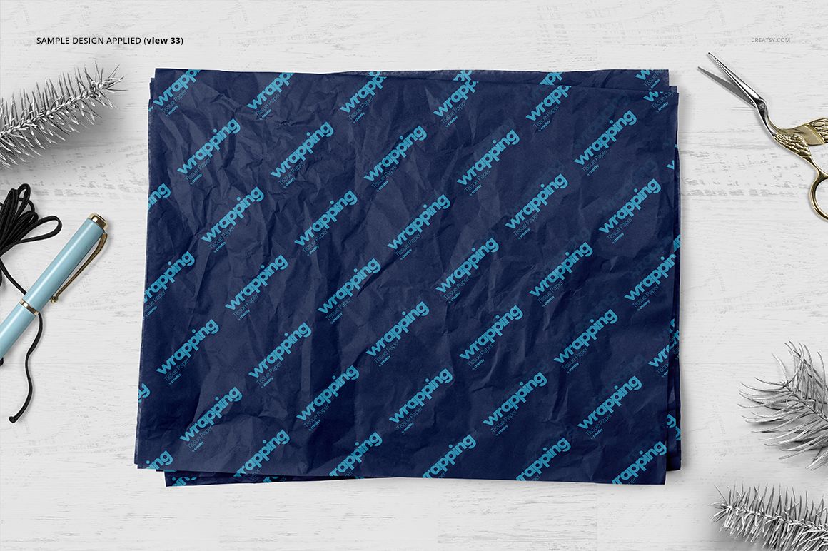 Front view of wrapping tissue paper mockup featuring dark blue sheets with repeated blue lettering, surrounded by props.