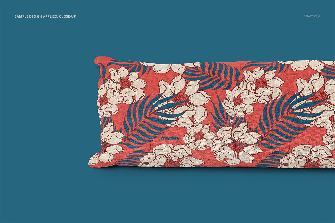 Close-up view of a long pillow mockup displaying bold red fabric with white flowers and blue leaves on a blue backdrop.