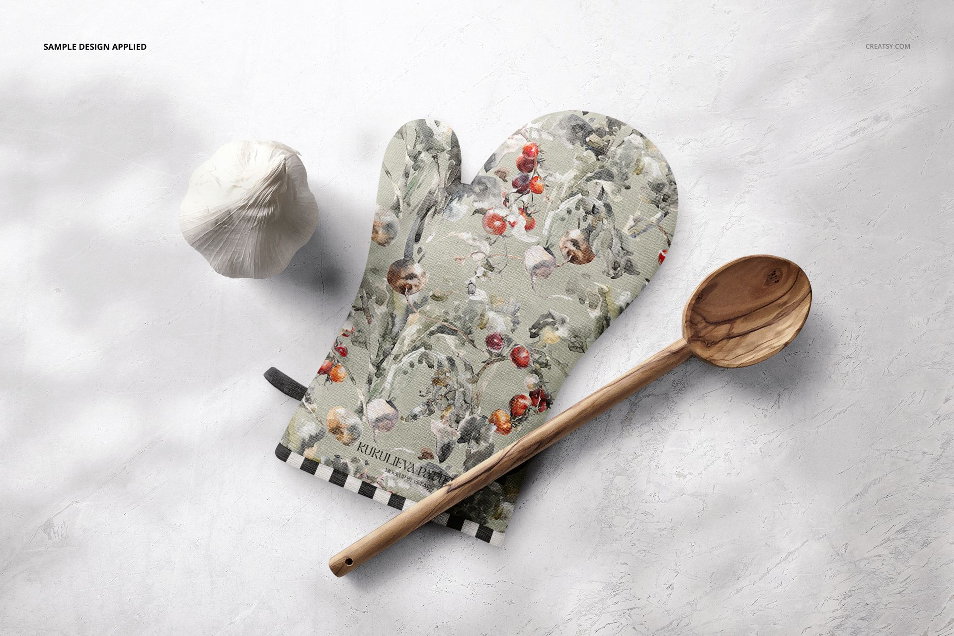 Floral-patterned oven mitt mockup shown from a top view, placed beside a wooden spoon and garlic on a pale background.