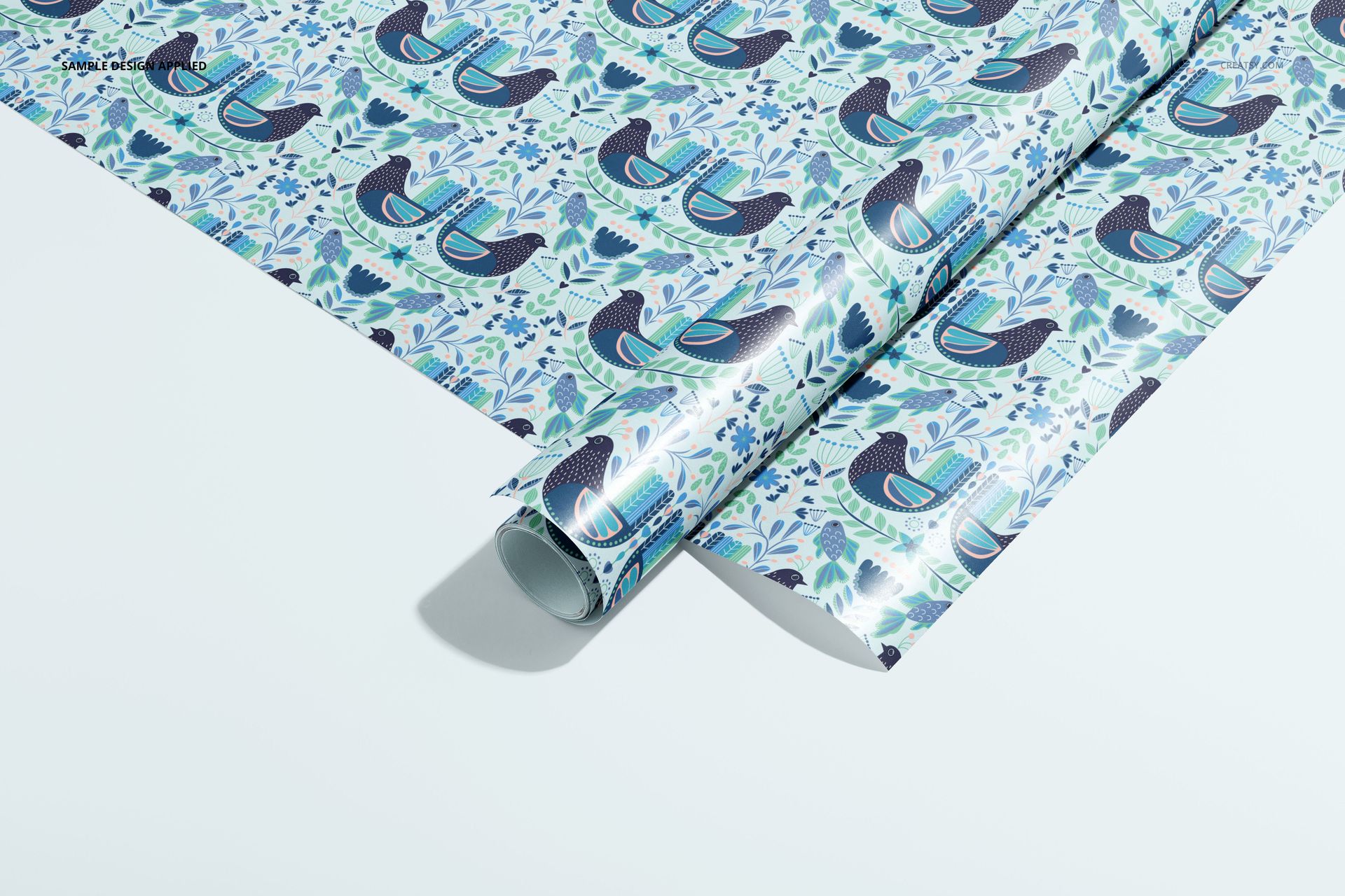 Gift wrapping paper mockup showing a roll and flat sheet with blue and green bird motifs and leafy accents.