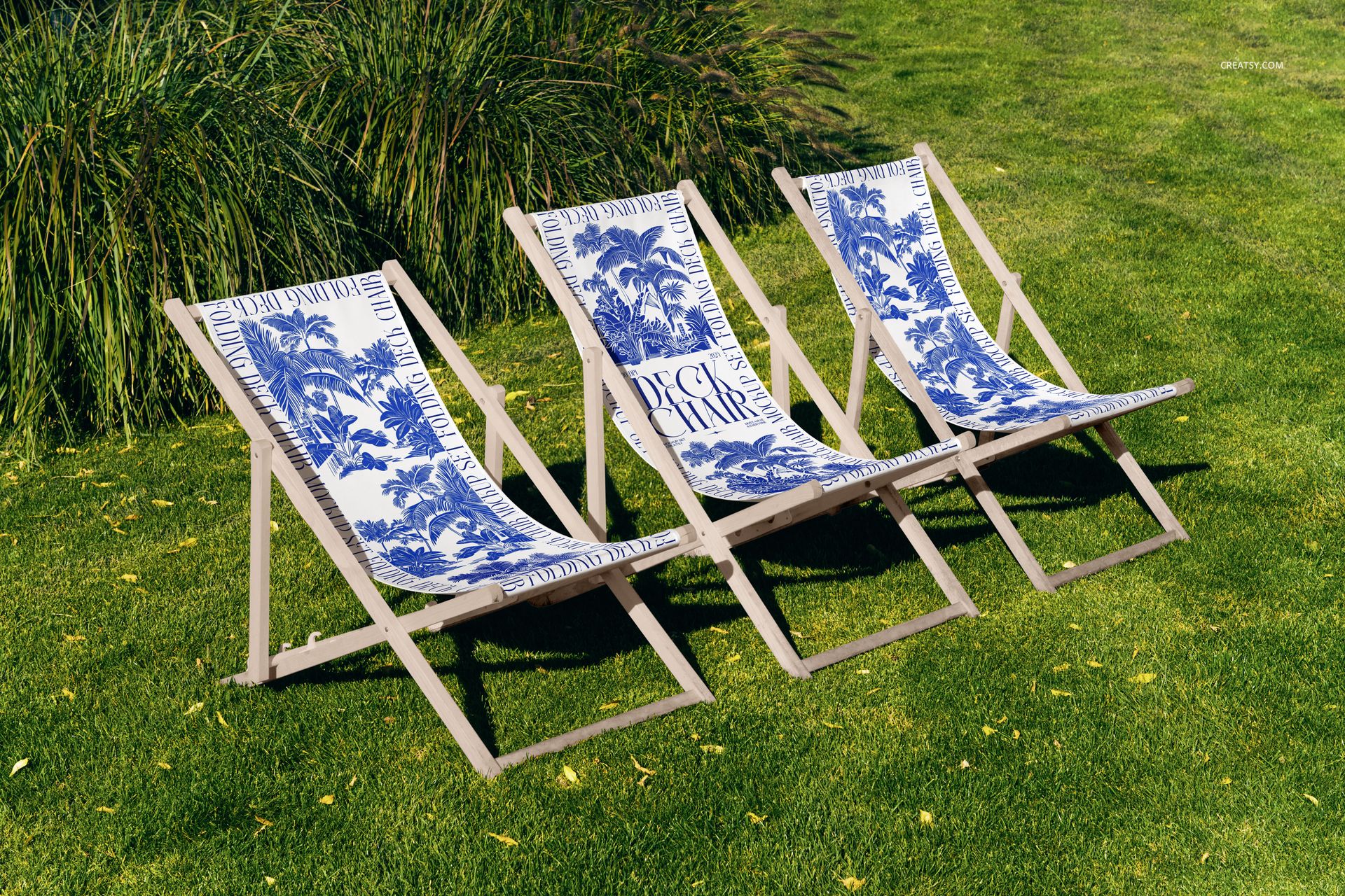 Outdoor scene showing three folding deck chairs with printed fabric, displayed as a mockup on a sunlit garden lawn.