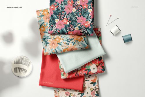 PSD mockup showing multiple folded fabric types in floral and plain designs, surrounded by sewing accessories on a table.