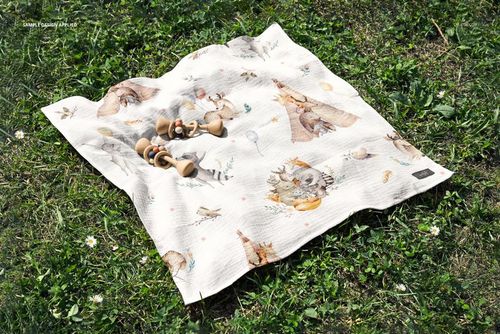 Top view of a crinkled muslin swaddle blanket mockup featuring playful animal designs and wooden rattles on grass.