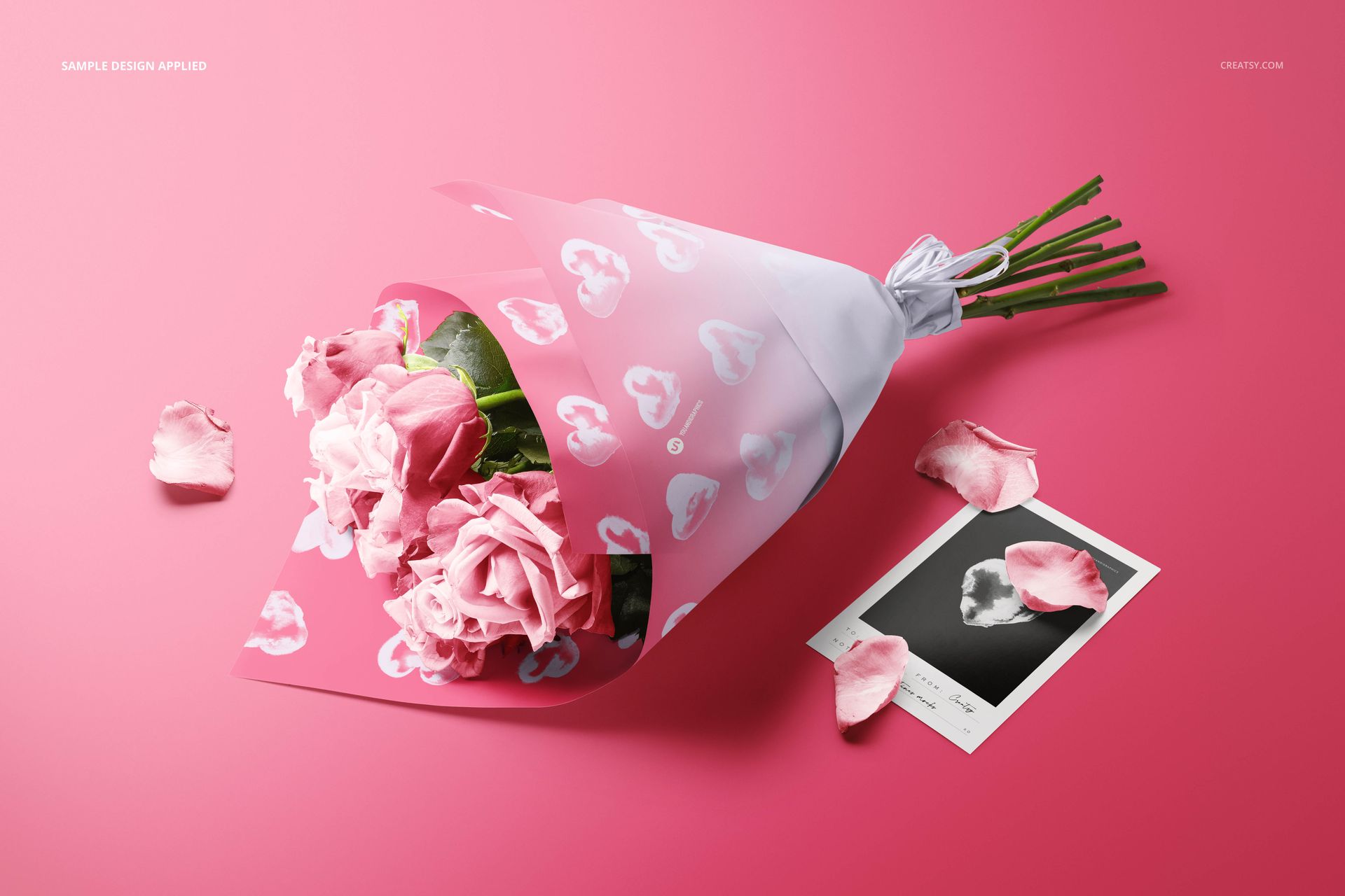 PSD mockup showing a bouquet of pink roses in decorative wrapping paper, with petals and a card on a pink backdrop.