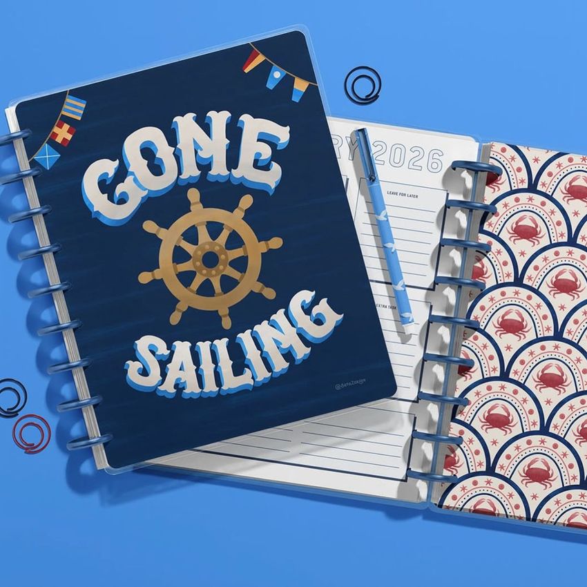 Top view of two spiral planners on a blue background, one with a nautical wheel and text, the other with a red crab pattern.