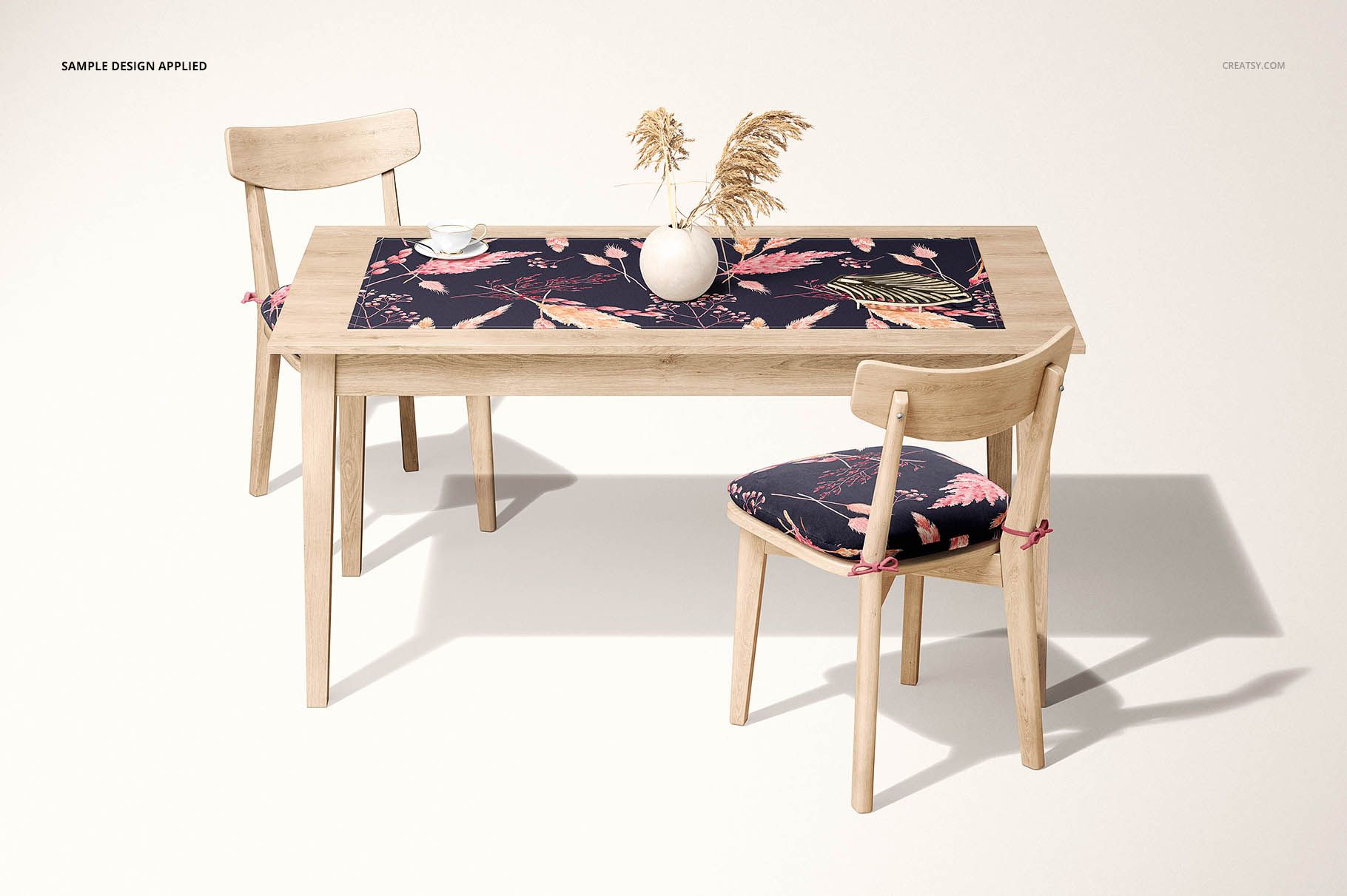 Table runner mockup displayed on a rectangular wooden table, decorated with botanical prints and a vase of dried plants.