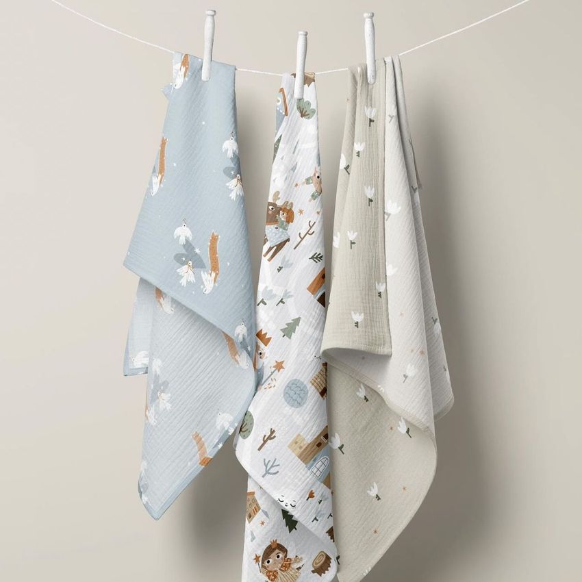 Swaddle blanket mockup with blankets draped on a string, displaying various illustrated woodland designs against a neutral wall.