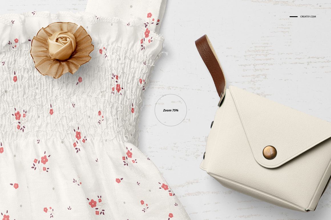 Top-down perspective of a white baby dress with pink flowers and a tan fabric rose, accompanied by a cream mockup bag.
