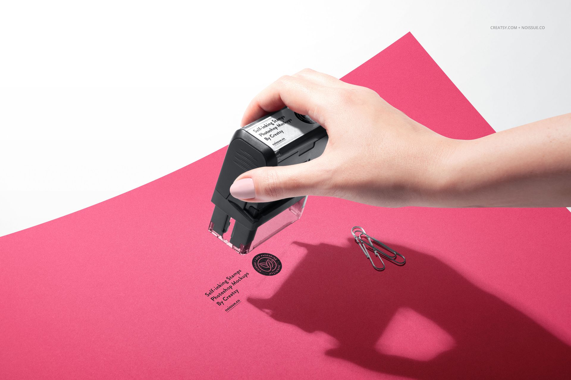 Close-up of a self-inking stamp mockup on red stationery, showing stamped design and scattered paper clips.
