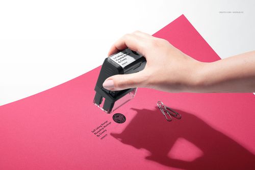 Close-up of a self-inking stamp mockup on red stationery, showing stamped design and scattered paper clips.