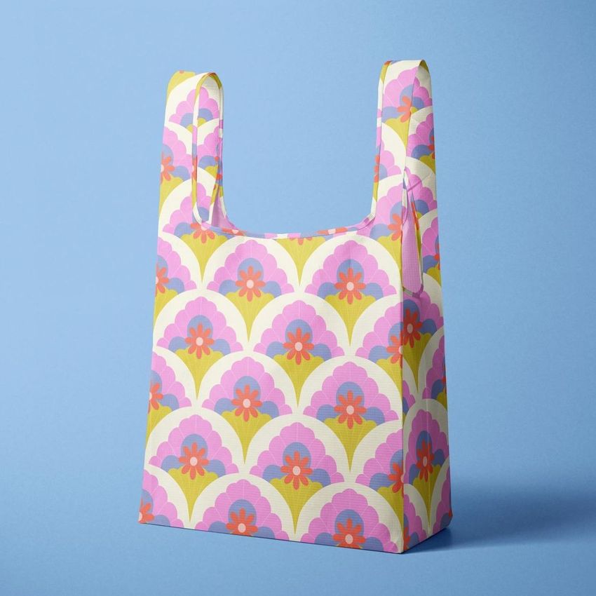 Reusable bag mockup featuring a retro geometric pattern with pink, purple, and orange flowers on a pale yellow background, set against a solid light blue backdrop.