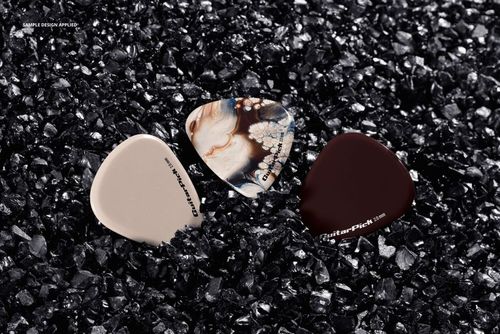 Guitar pick PSD mockup set with three picks nestled in crushed black stone, highlighting their unique appearances.