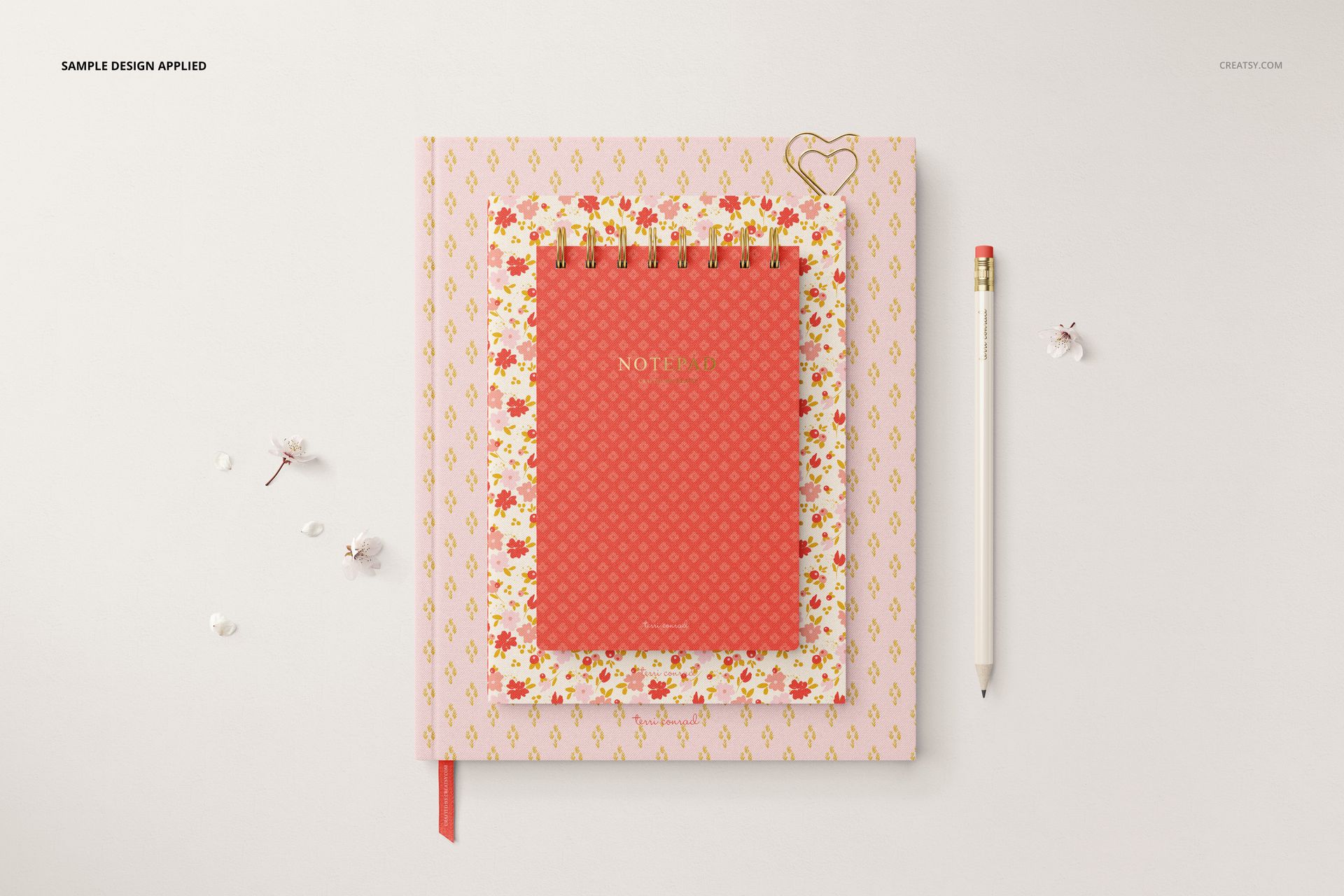 Top view of a stationery mockup bundle featuring a red spiral notebook, floral folder, and white pencil on a desk.
