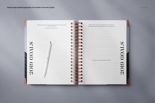 Wire-bound planner mockup with open pages, copper spiral binding, and a white pen on a light gray surface.