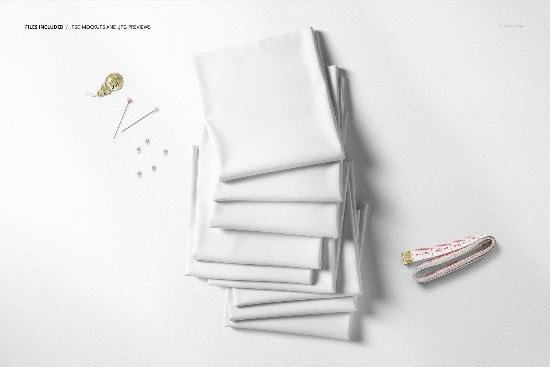 Top view of a fabric stack mockup featuring neatly folded white textiles and scattered sewing accessories.