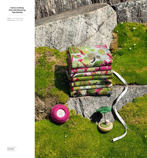 PSD mockup showing colorful floral fabric stack outdoors on mossy stone, with sewing props and measuring tape beside.