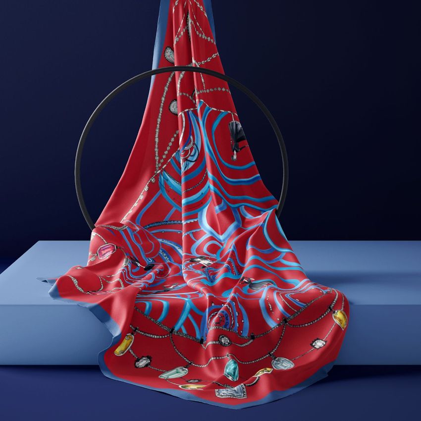 Silk scarf mockup draped over a geometric stand, featuring abstract red and blue patterns with jewel illustrations on a blue background.