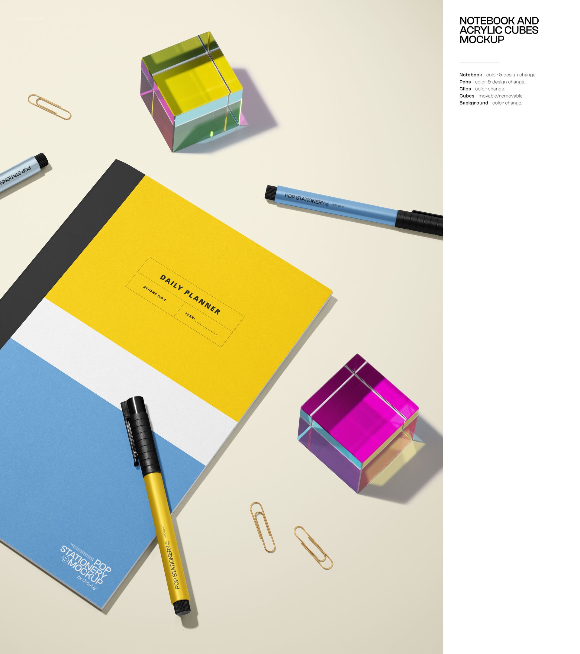 Stationery mockup featuring a notebook, two pens, paper clips, and multicolored acrylic cubes arranged on a pale surface.