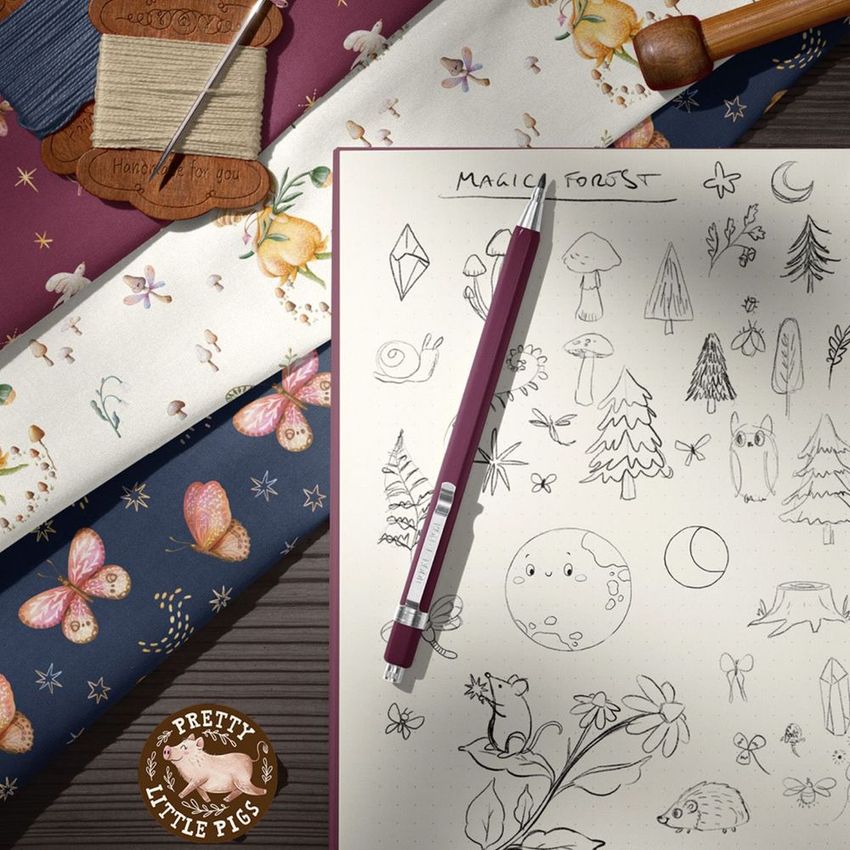 Cotton fabrics mockup featuring floral and butterfly patterns beside a sketchbook with forest-themed doodles and a pen.