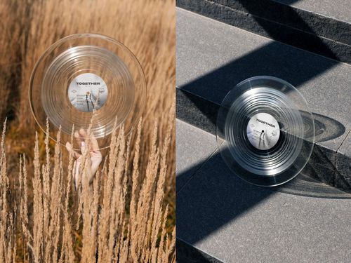 Transparent vinyl record mockup shown outdoors, featuring a hand in grass and a record resting on concrete steps.