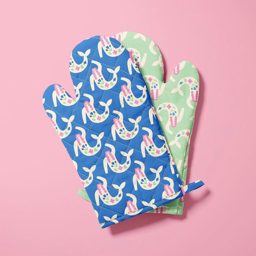 Oven mitt mockup featuring two mitts with playful mermaid patterns, one in blue and one in light green, on a pink background.