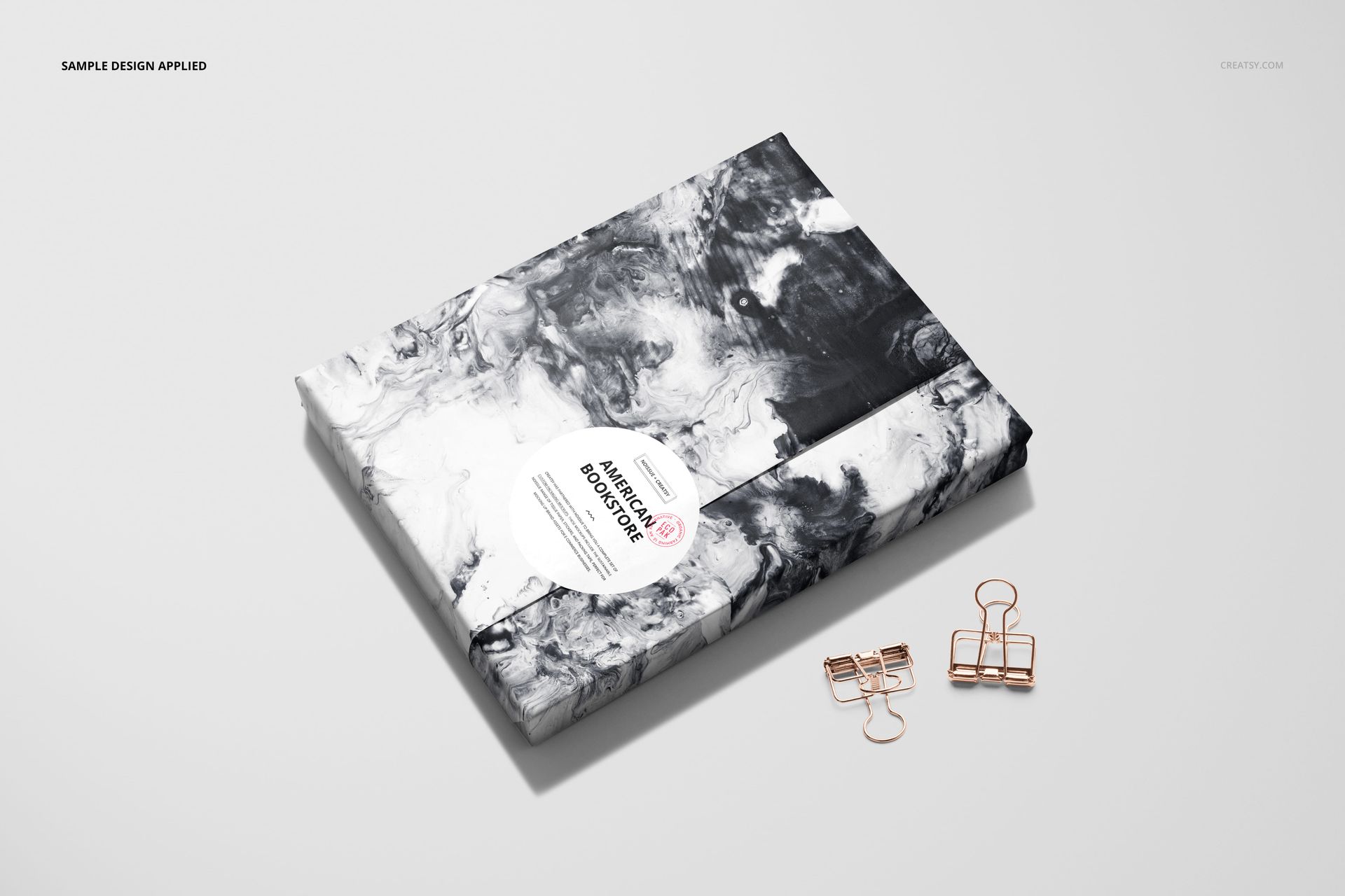 PSD mockup of a book covered in abstract black and white wrapping paper, displayed on a plain background with binder clips.