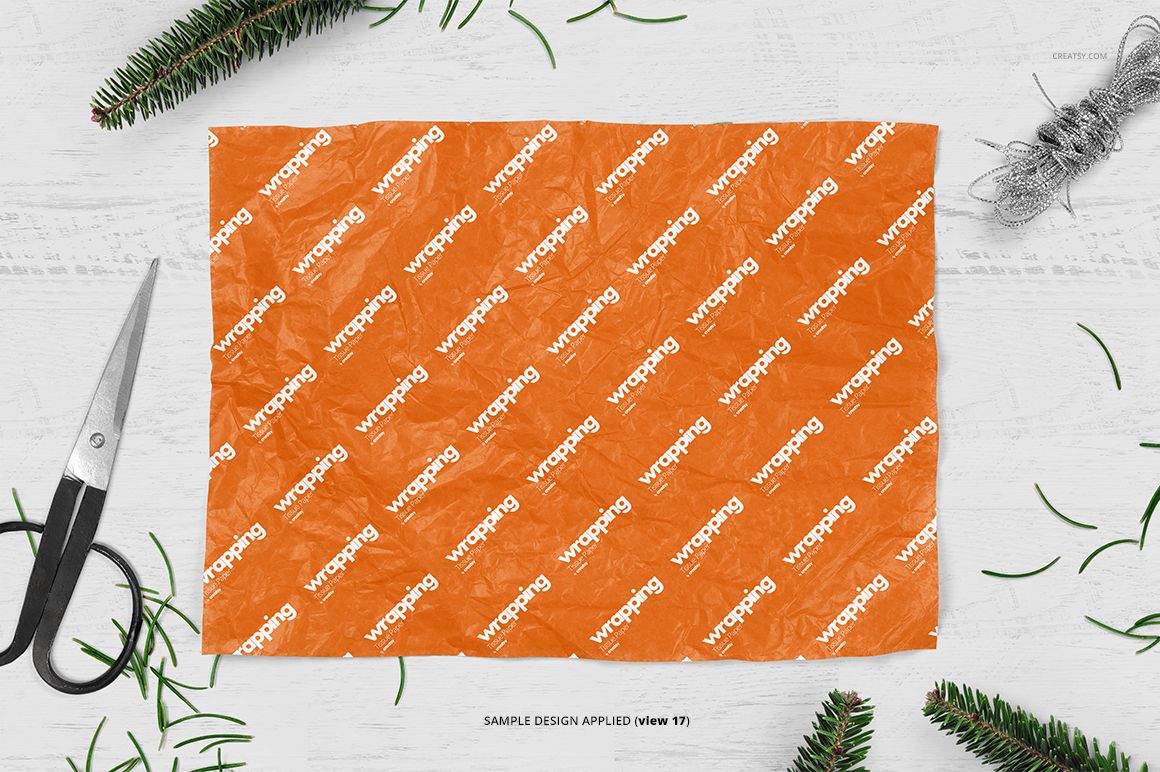 Top view of orange wrapping tissue paper mockup with repeated white text pattern, surrounded by green pine branches.