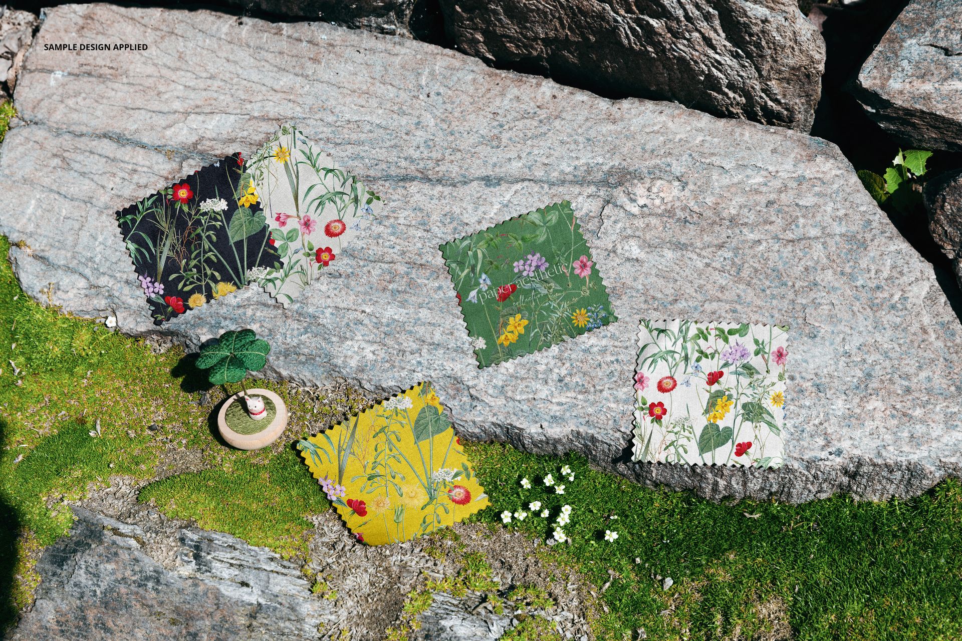 PSD mockup featuring floral fabric samples laid out on a textured stone surface with greenery and tiny flowers nearby.
