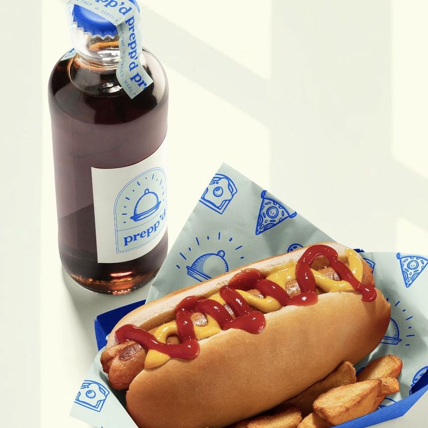 Hot dog with ketchup and mustard in a blue patterned food safe paper mockup, served with potato wedges and a drink bottle on a light surface.