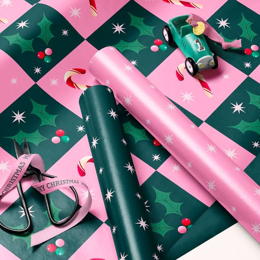 Gift wrapping paper mockup featuring pink and green sheets with holly, candy cane, and star patterns, shown with scissors and a toy car.