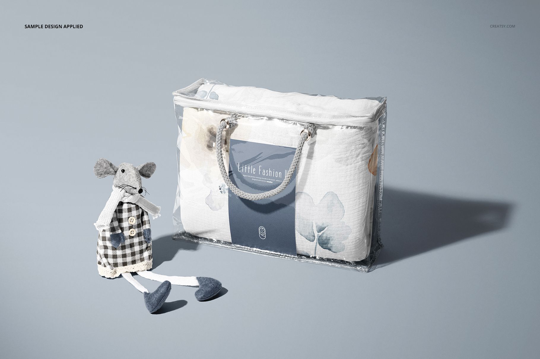 Newborn swaddle wrap mockup displayed in a clear plastic bag with a blue label, next to a soft fabric mouse toy.