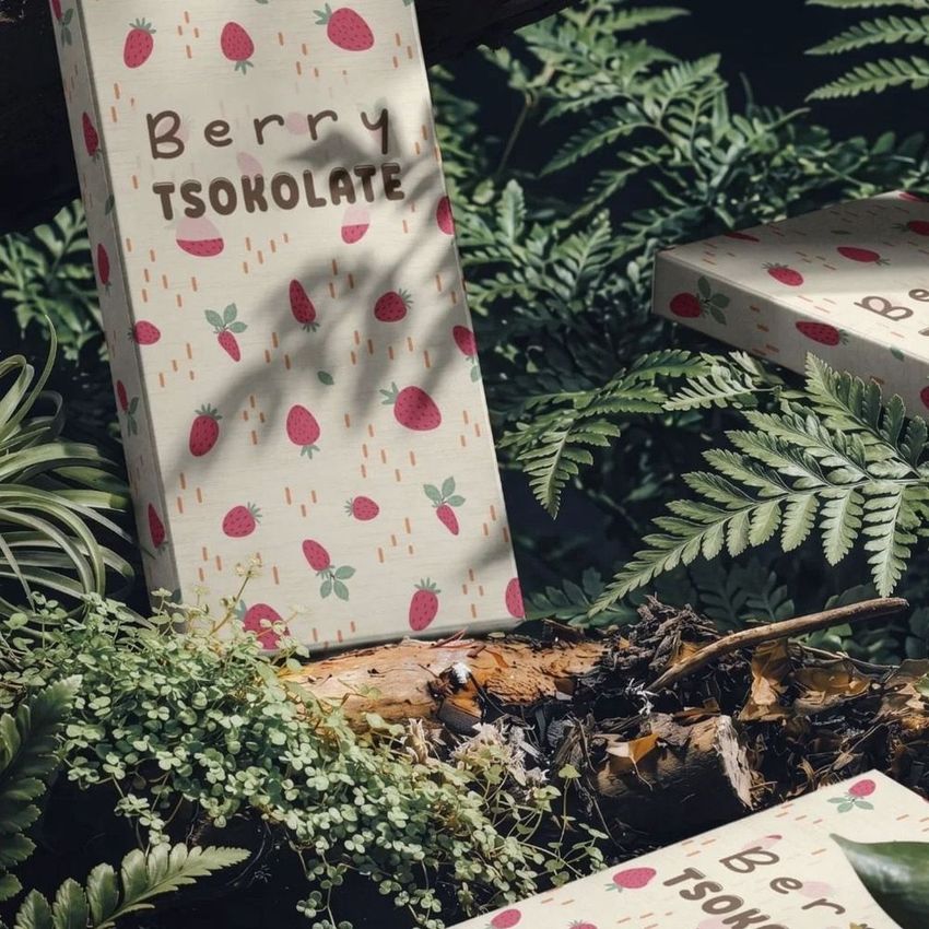 Chocolate box mockup featuring strawberry-themed packaging placed among green ferns and forest foliage in natural light.