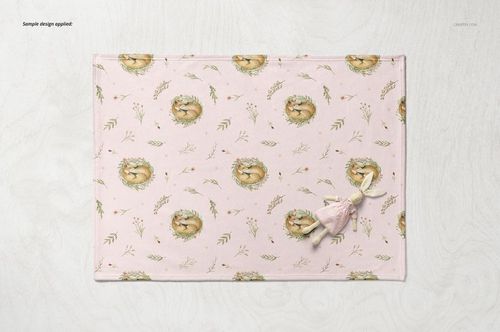 Soft fleece baby blanket mockup with a pink background, illustrated animal pattern, and a small doll on top.