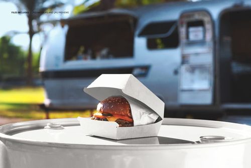 Open burger box mockup on a round barrel, featuring a visible burger and a silver food truck in the background.
