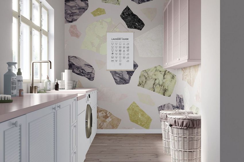 Laundry room mockup showing a pastel terrazzo-patterned wall, washing machine, cabinets, wicker baskets, and a laundry guide poster.