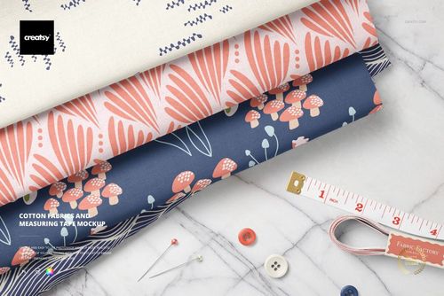 Cotton fabrics in floral and abstract designs, arranged on a marble tabletop alongside a measuring tape, pins, and buttons in a PSD mockup.