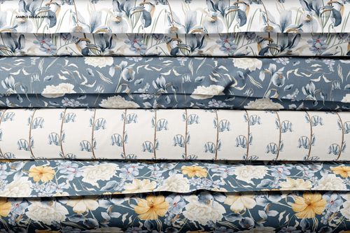 Stacked rolls of fabric with various floral patterns in blue, white, and yellow tones, viewed from the front.